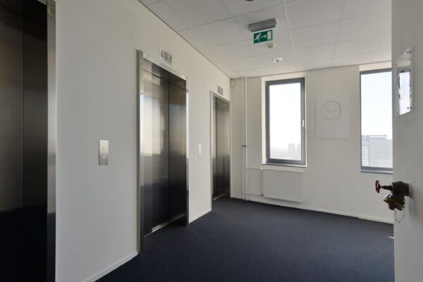 Liftlobby op de negende verdieping van het kantoorgebouw aan de Laan van Zuid Hoorn, met drie liften en uitzicht op de stad.
